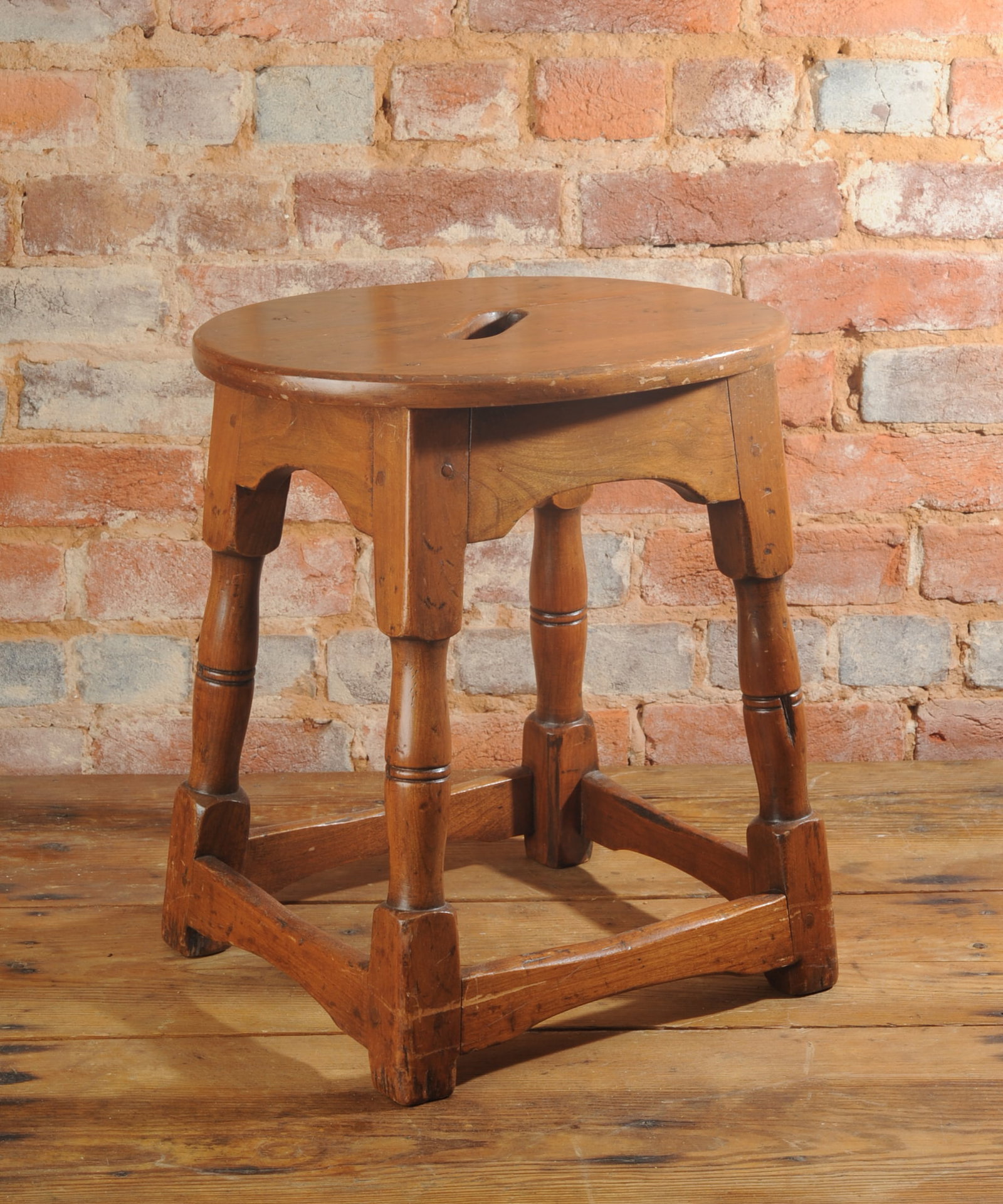 Country Milking Stool: Stool constructed with an oval wooden seat featuring a centered hand grip cutout raised on four turned legs joined by box stretchers, early to mid 20th century. H: approx. 17 1/4". Seat: approx. 15 1/