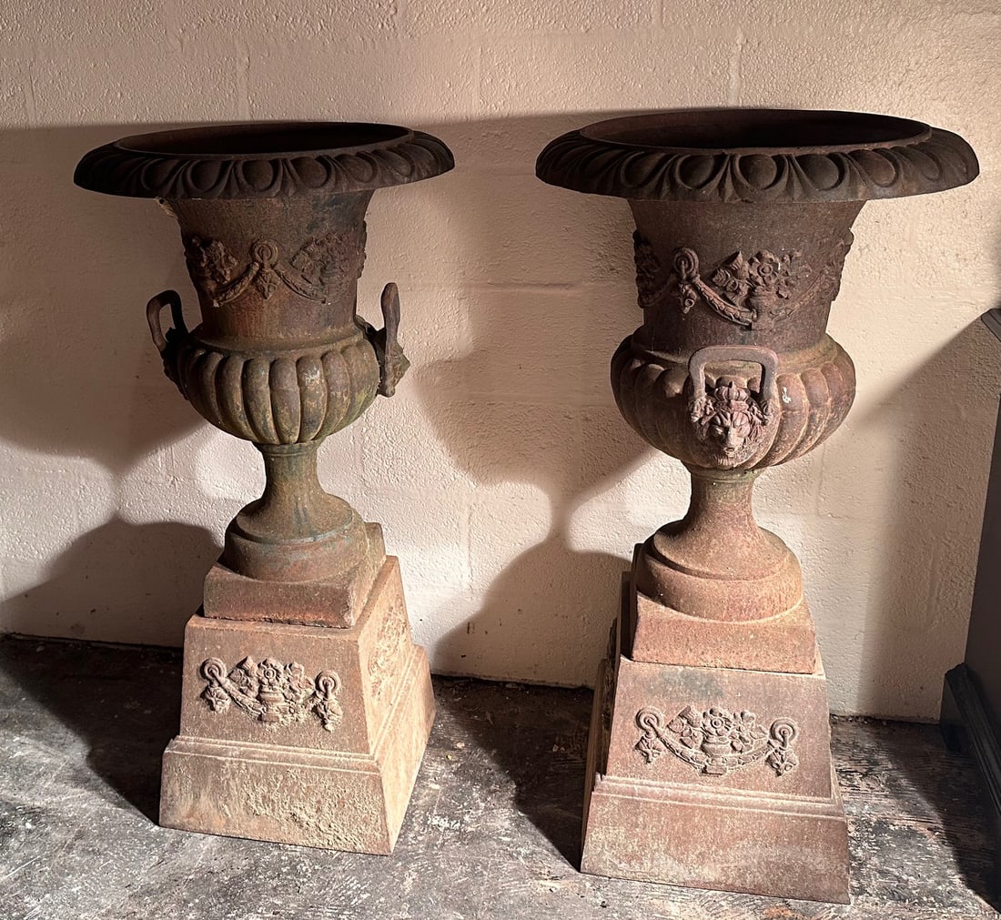 Pair of Cast Iron Garden Urns with Pedestal Bases: Possibly French or Continental, substantial pair of cast iron garden urns, each of campana form with wide gadrooned rims above flaring bodies, cast in relief with classical swags, masks, and ribboned
