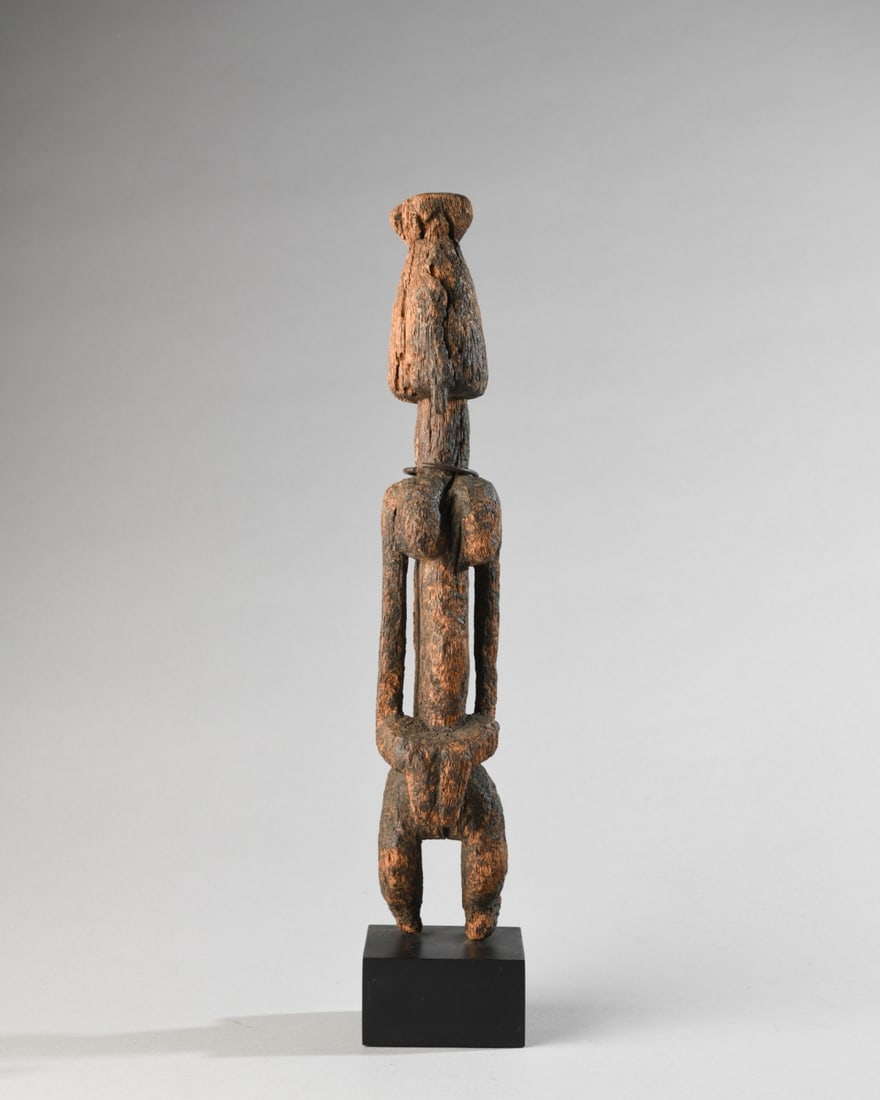 Dogon Female Figure, Mali: Dogon female figure with top knot, elongated face and torso, squared, narrow shoulders, arms carved parallel to the body, bent at the elbow, hands away from but covering the genitals. standing