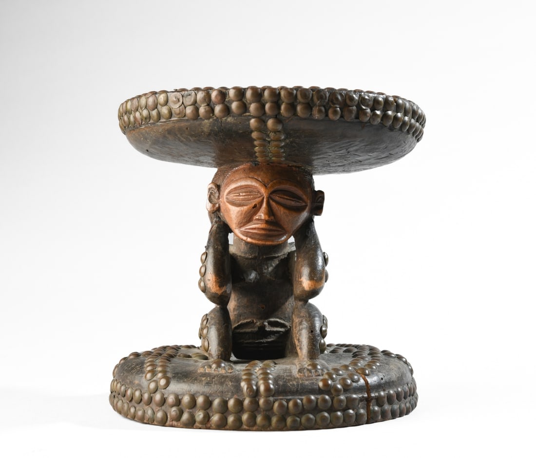 Early 20th C. Chokwe Stool, Ex-Sotheby's: Ceremonial Chokwe figural stool, the round top supported by a kneeling young female figure on a round base, the whole of carved hardwood with brass stud detail. The figure is well carved, with