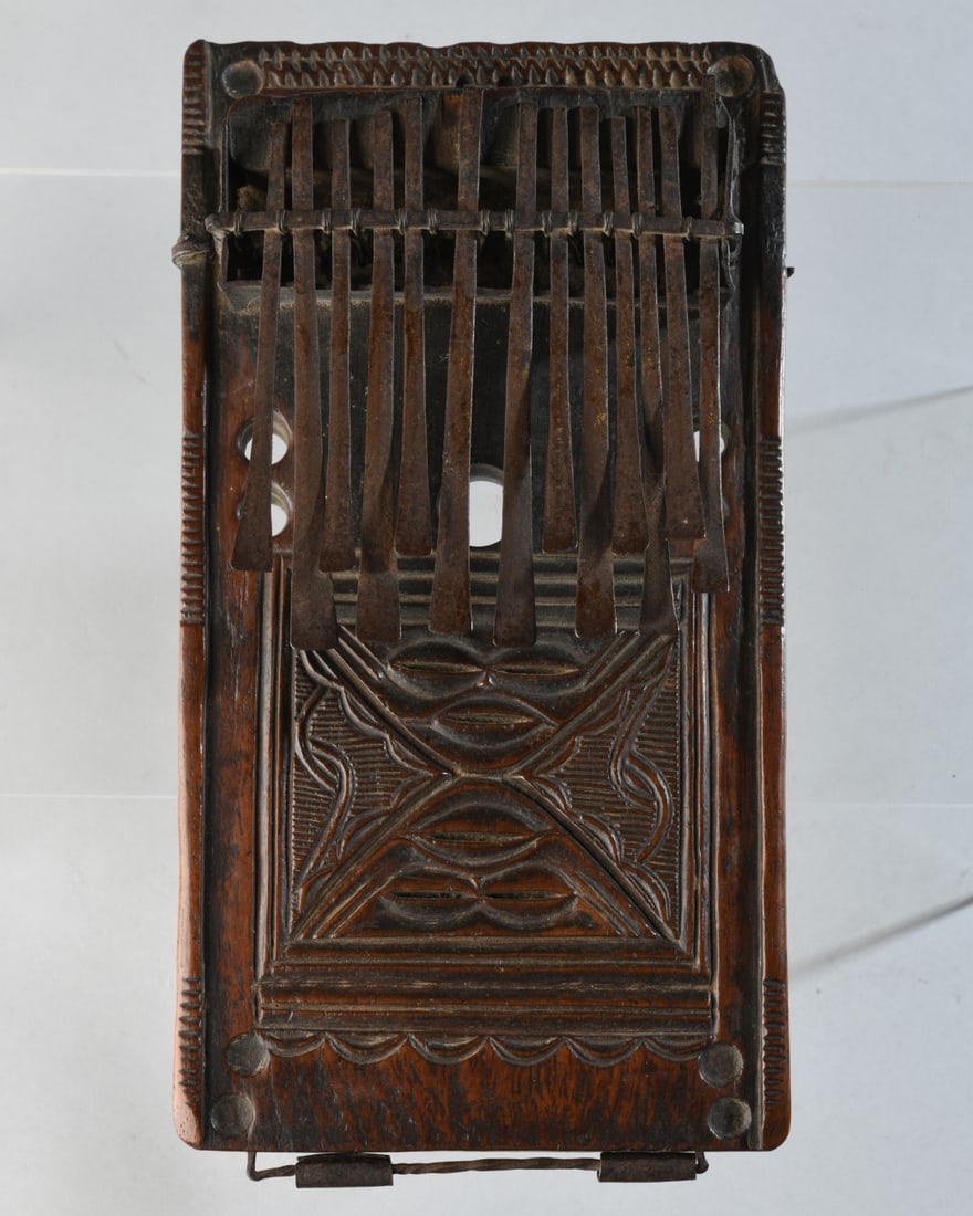 19th C. Lwena / Chokwe Thumb Piano, Ex-Christie's: Lwena or Chokwe sanza, the face with thirteen keys mounted to original sound box and mounted to hardwood panel finely carved with a pair of inverted masks on the face and with curved and geometric mot