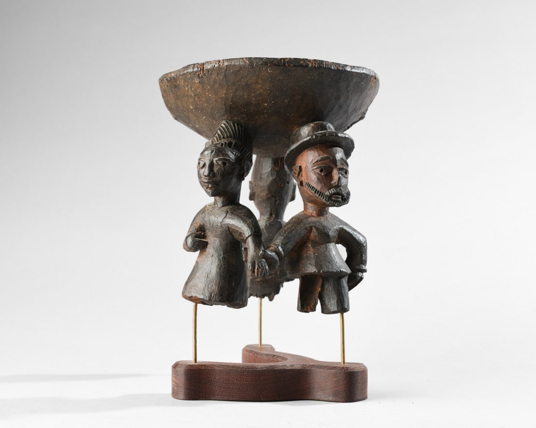 Yoruba Ifa Divination Bowl (fragment): Small divination bowl carved in one piece with the three figures upon whose heads it rests. Two of the figures appear to be a couple, both in colonial clothing; the female in a dress, the male in a