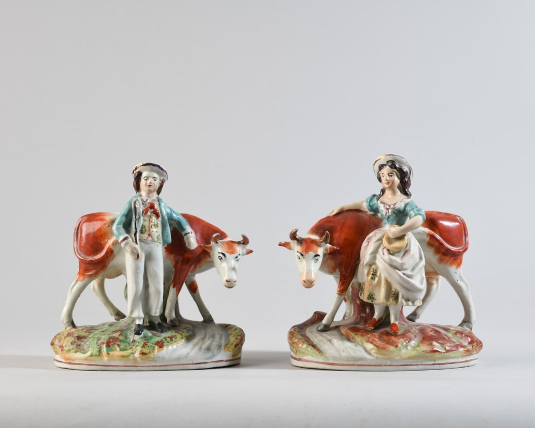 Pair of Staffordshire Figural Groups: Pair of Staffordshire figural goups of a cowherd and milkmaid. Each modeled standing beside a red-and-white cow on a naturalistic base, the male figure holding a stick and the female holding a milk