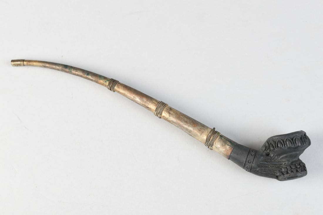 Carved Wood & Brass Figural Pipe: Carved blackened wood bowl with raised foliate and linear decoration and a short cylindrical cup, fitted to a curved brass stem with applied coiled wire bands (several loose / disconnected); likely Af