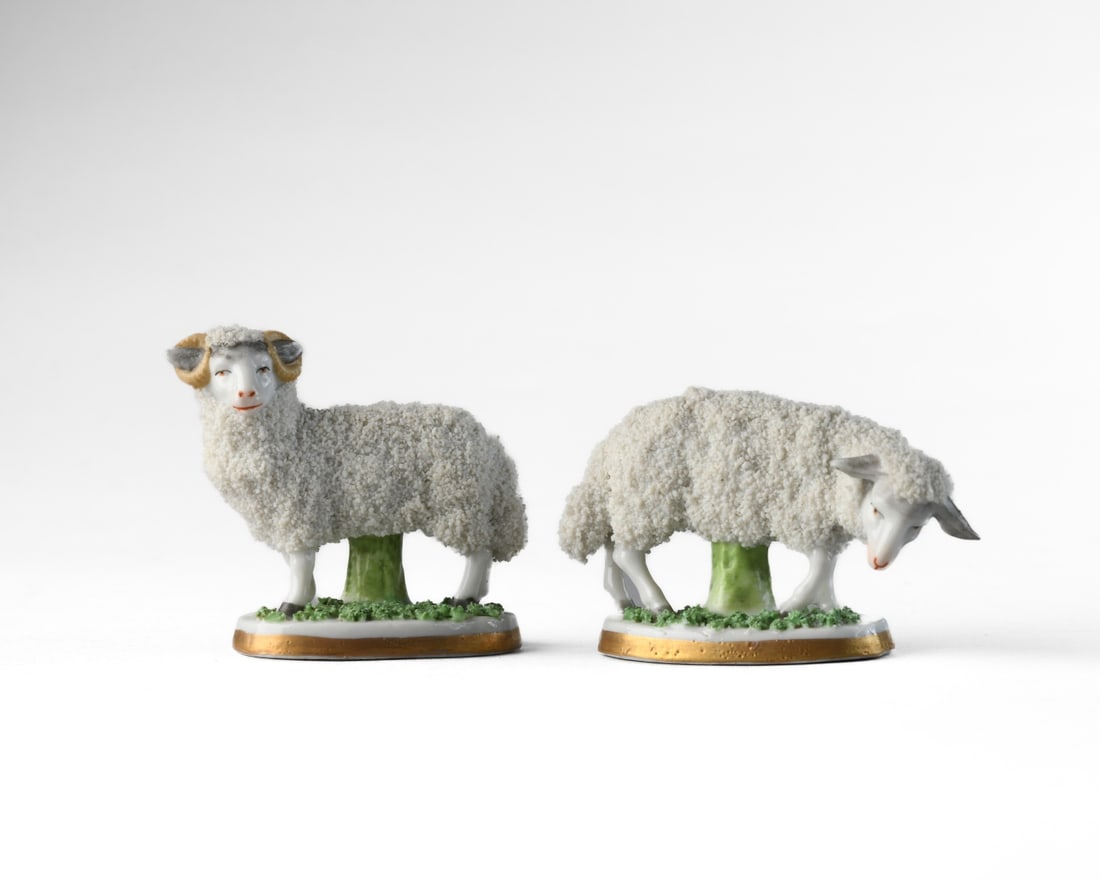Pair of Chelsea-Style Porcelain Sheep: Early 20th century, sheep modeled standing with heads lowered, the bodies richly encrusted with applied granular “wool,” raised on oval bases with gilt rims and anchor marks. No visible chips,