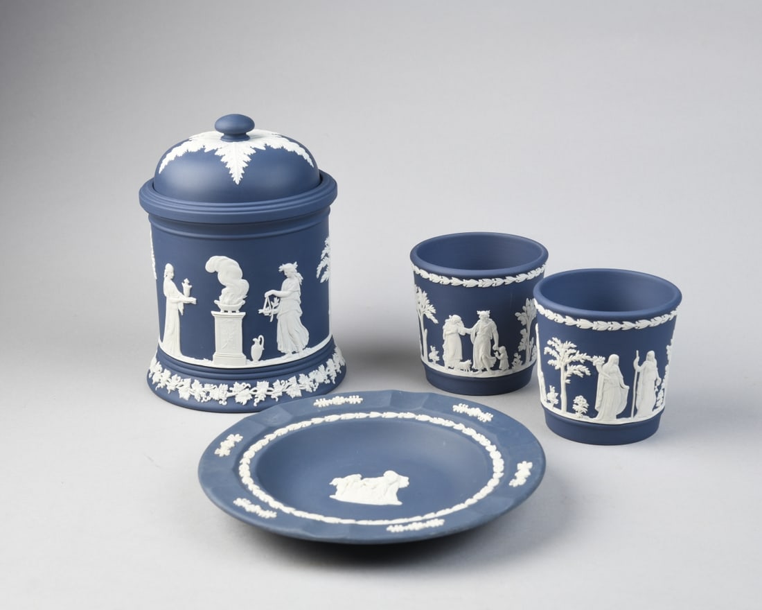 4 pcs. 20th C. Wedgwood Jasperware: Blue jasperware group including a covered jar, a pair of cups and a small plate, each with applied white neoclassical figural reliefs and foliate borders, 20th century, marked to undersides, no