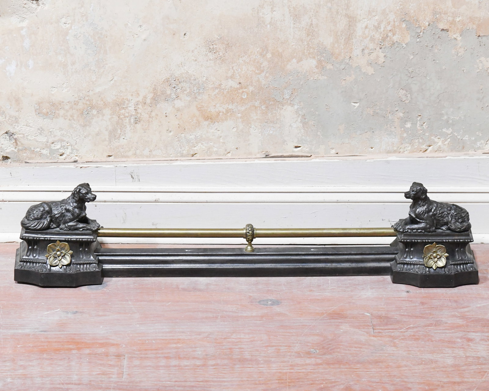 20th C. Victorian Style Fireplace Fender: Rectangular form with a brass rail supported by central mount, the ends cast with recumbent dog figures atop plinth bases, black-painted iron base, some minor surface wear, oxidation and rust.Approx.