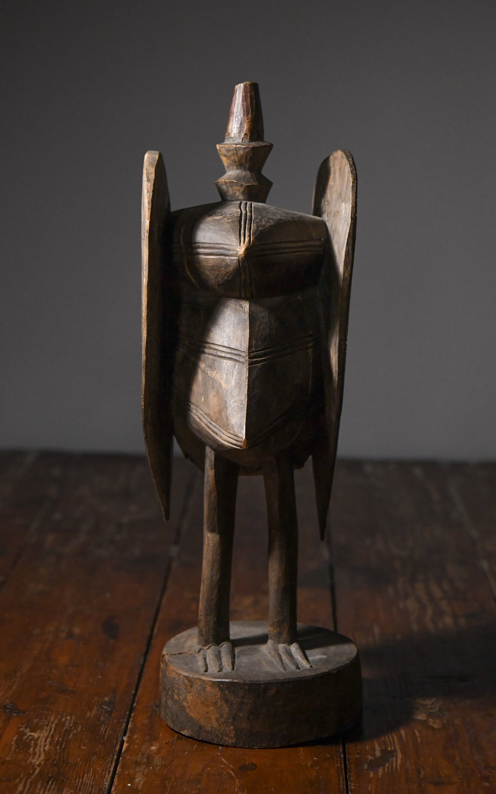 20th C. Carved African Bird Figure: Probably West African, stylized bird with geometric body, elongated beak, and upright crest, the wings rendered as flat, vertical panels with incised linear decoration; surface with dark, worn patina 