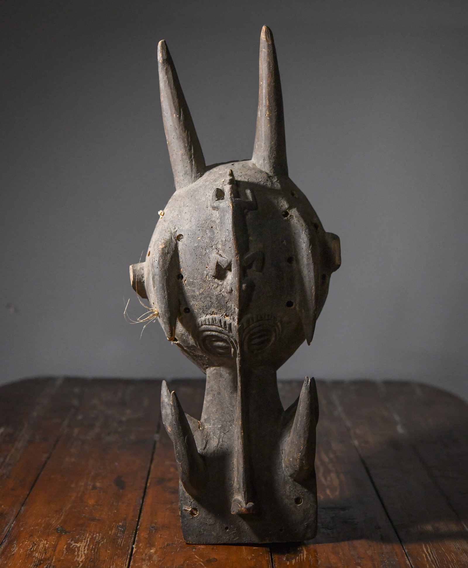 West African Carved Helmet Mask: With projecting horn-like elements, stylized facial features, surface with dark, encrusted patina and scattered insect damage; extensive wear including losses at the rim, perforations, and abrasions t