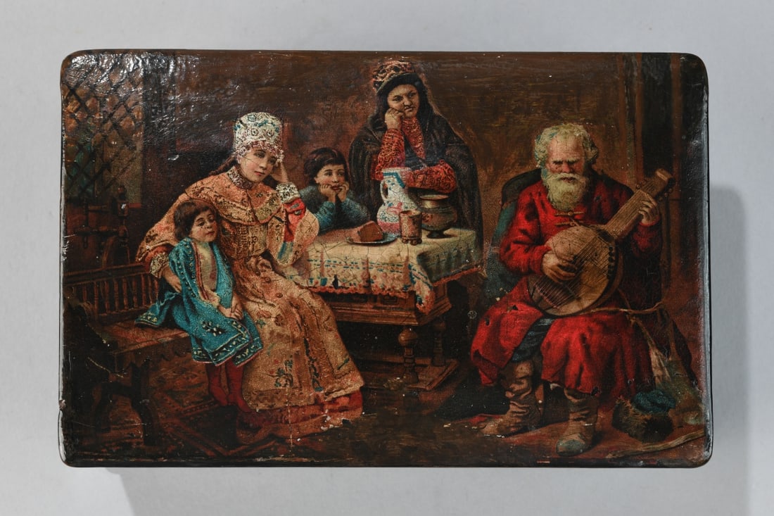 Lacquered Russian Box with Genre Scene: With hinged lid, the top decorated with a printed and varnished scene of a seated family group with a musician in Russian dress, the interior and underside in black lacquer, 20th century; surface