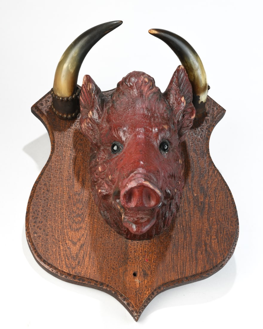 Carved & Painted Wooden Boar's Head Mount: 20th century, head with inset glass eyes, mounted on a shaped oak-form backboard and fitted with curved horn elements (one loose) and metal suspension chains. Surface wear, abrasions, and scattered pa