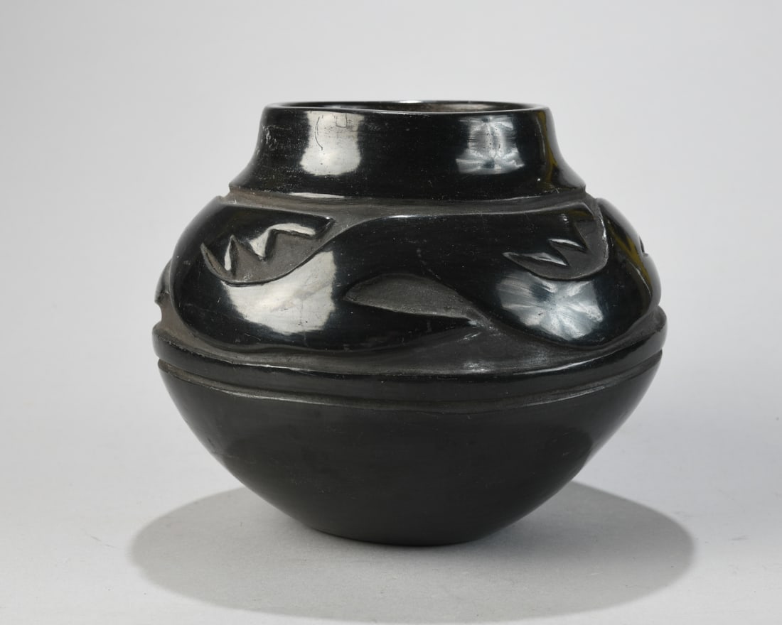 Santa Clara Pueblo Carved Blackware Jar: Globular form with short everted neck, the shoulder deeply carved with a continuous avanyu (water serpent) motif above a raised banded foot, stone-polished to a black luster. Signed in script on the