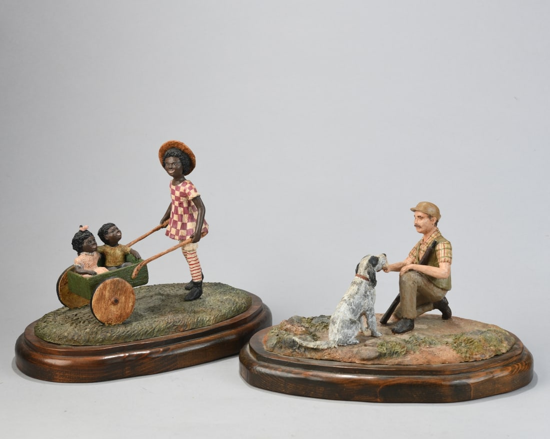 2 Meredith Rambo (US, 20th C.) Figural Groupings: Carved and polychrome-painted figures on shaped wooden plinth bases. One depicting a kneeling male hunter holding a rifle, interacting with a seated dog; the other showing a girl pulling two children
