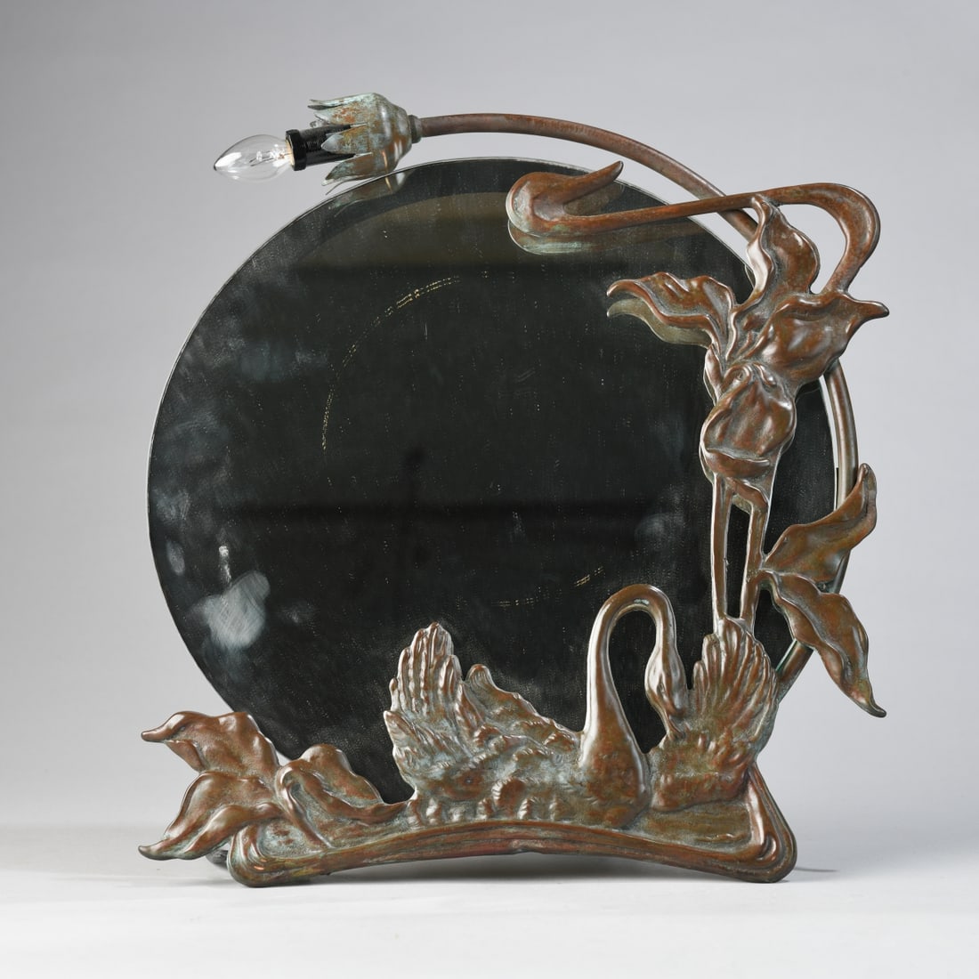 Art Nouveau-style Figural Lighted Mirror: Cast metal frame with brown patina, modeled with swans and sinuous foliate forms around a circular mirror, fitted with a single socket and cord (powers on); unmarked. Mid to late 20th century, in the 