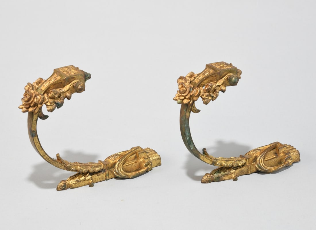 Pair of Bronze Curtain Tiebacks: Cast bronze with foliate and classical revival decoration, each with scrolling arm and wreath-form mount; stamped “R L 210” verso. Minor surface wear. Dimensions approx. 6" D x 6 3/4" H x 2