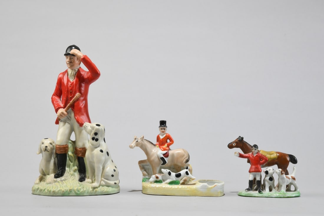 Three Porcelain Hunting Figures: Comprising a larger unmarked polychrome figure of a huntsman in a red coat flanked by two hounds, together with two smaller Japanese export porcelain figures of riders and attendants with dogs and