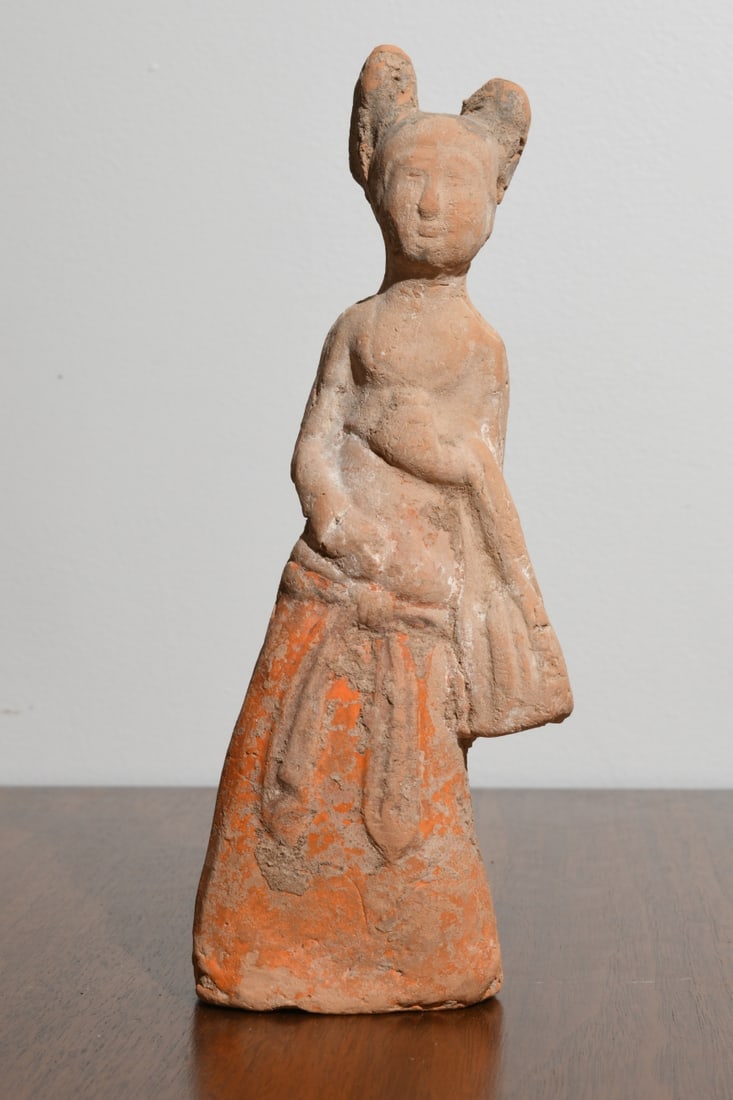 Chinese Pottery Female Figure, Tang Style: Earthenware with orange pigment and surface encrustation, the standing figure modeled as a court lady with high coiffure and long skirt, holding a draped sleeve or bundled object at the waist, hollow 