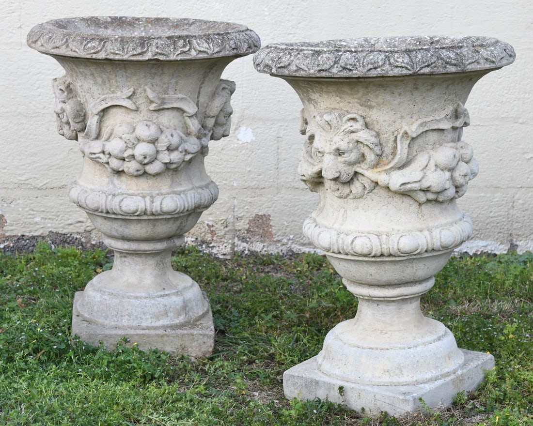 Pair of 20th C. Garden Urns: Neoclassical style concrete garden urns with lion's head motif and fruiting garlands, weathered patina with minor chips and abrasions. Dimensions approx. 26 1/2" H x 19" dia. Our primary recommendatio