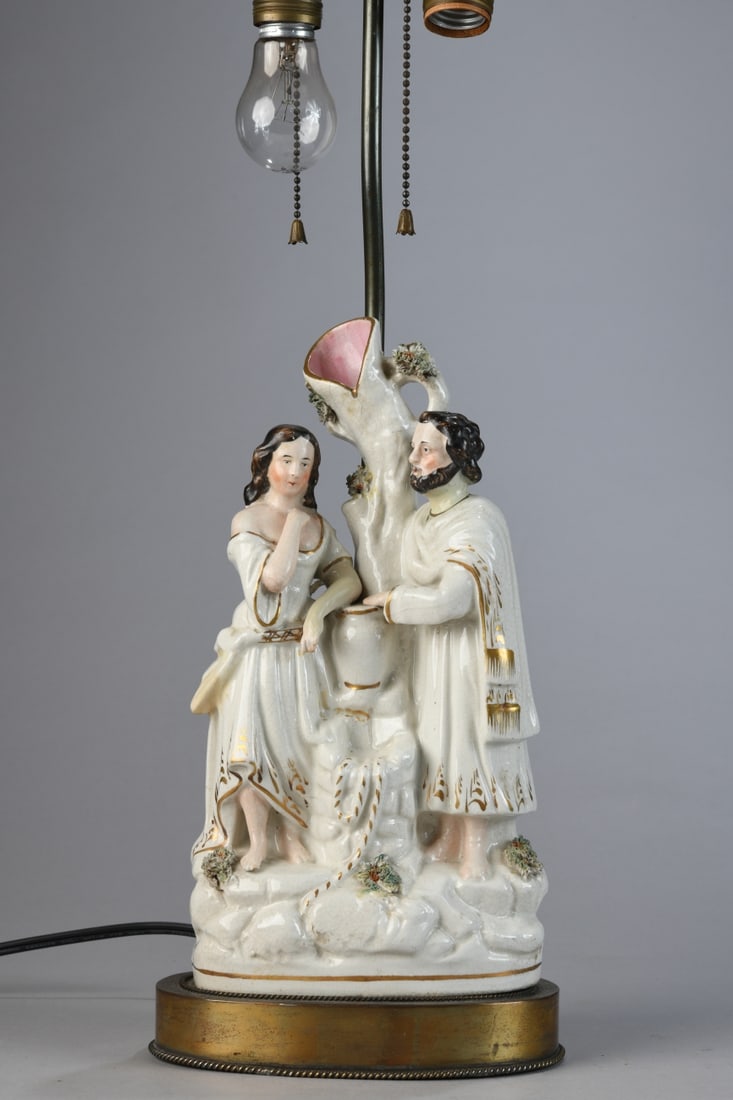 Staffordshire Spill Vase Lamp: Glazed porcelain group depicting a courting couple beside a tree form fountain or vase, with gilt accents and applied floral decoration, mounted on an oval metal base with twin light sockets and brass