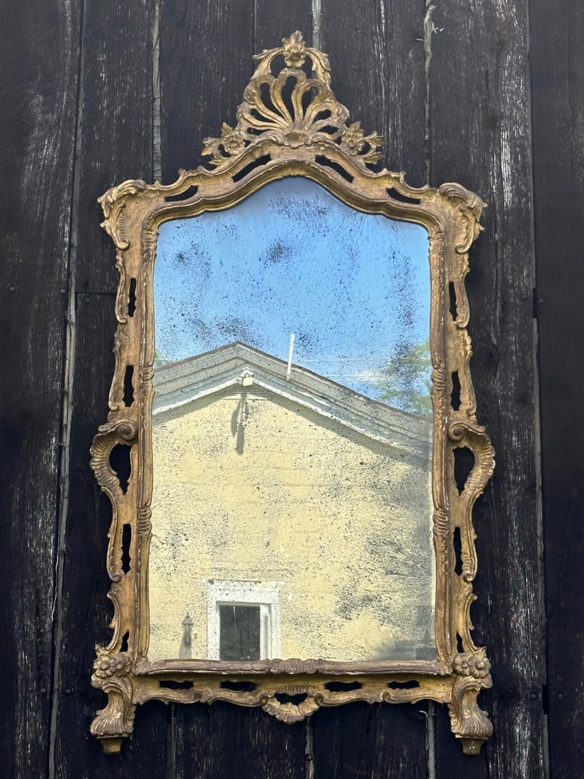 Continental Rococo Style Giltwood Mirror: Carved giltwood wall mirror with shaped arched mirror plate, pierced foliate crest, scrolling side supports, floral ornament, some silvering loss and spotting to mirror, scattered chips, cracks and