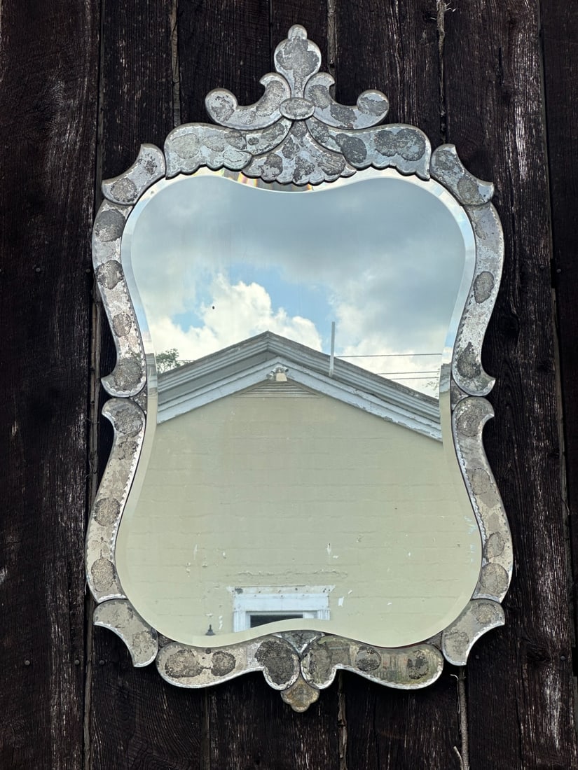 20th C. Venetian Style Mirror: Shaped wall mirror with beveled central mirror plate and applied mirrored glass frame with scrolled crest and foliate-form decoration. Some silvering loss, spotting, oxidation, and losses to backing,