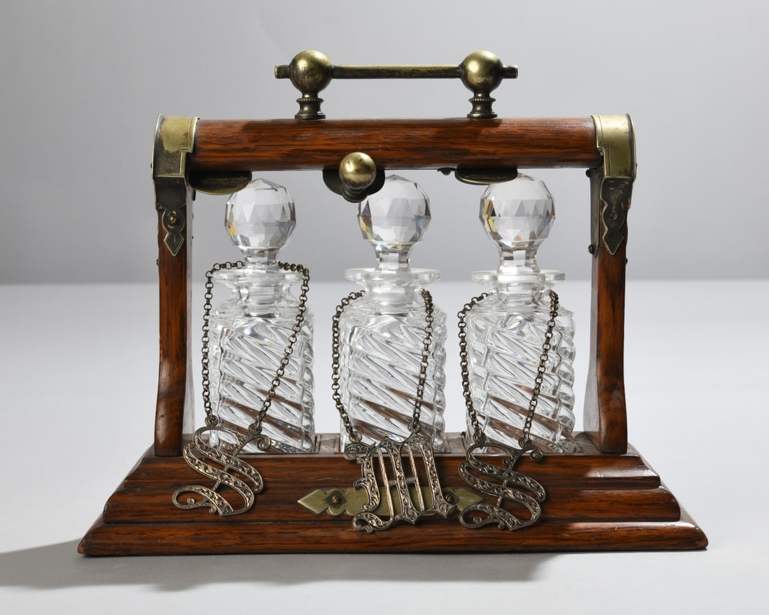 Victorian Oak Tantalus: Compact form, fitted with three glass decanters, engraved brass mounts, and hanging liquor labels. Dimensions approx. 8" 9 7/8" x 4 1/4". Our primary recommendation is to arrange shipping yourself