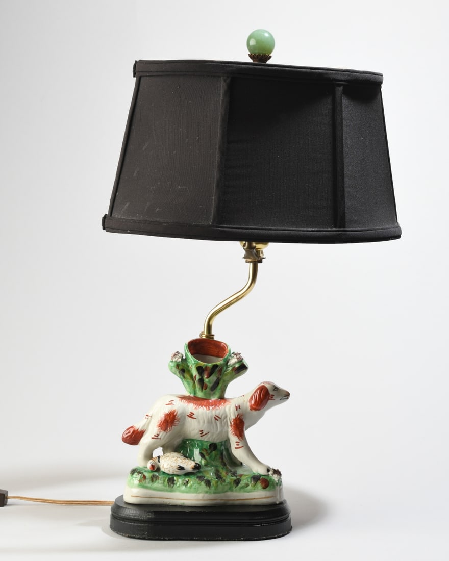 Staffordshire-Style Spaniel Figure Table Lamp: 20th century, spaniel standing before a tree stump with a bird at its feet, mounted as a table lamp on a shaped black wood base with brass-tone standard and socket, lamp powered on when tested.f H:
