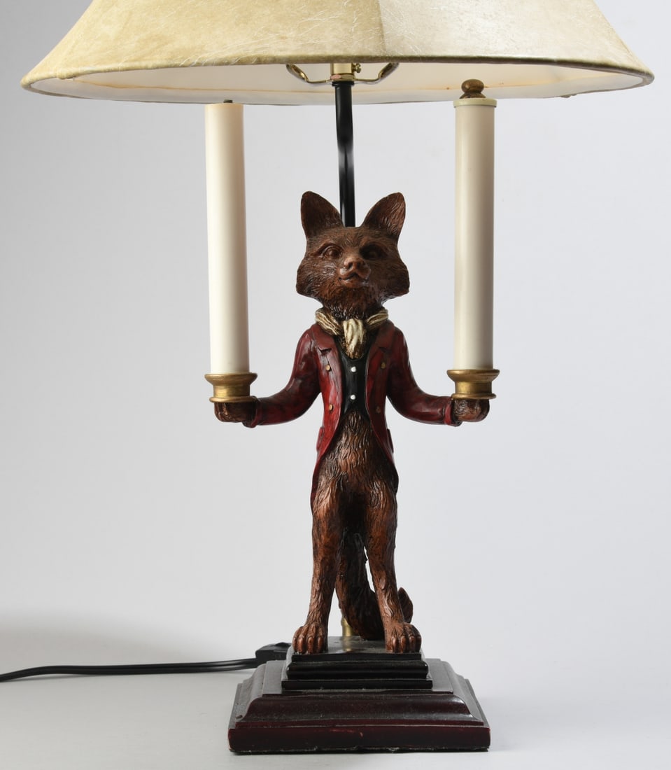 Contemporary Fox Form Table Lamp: Modeled as a fox standing upright and dressed in a red coat and scarf, supporting two faux candle forms (one missing its upper cap), mounted to a stepped rectangular base. Lamp powered on when tested.