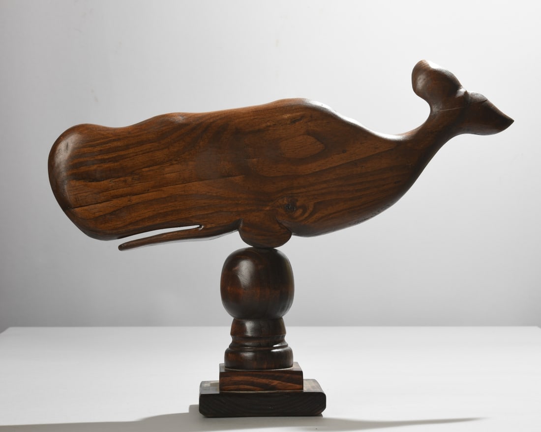 Lindsay Jones (American, 20th/21st C) Carved Whale: Hand carved and dark-stained wood sculpture depicting a whale in streamlined profile, mounted on a turned pedestal and stepped square base. Signed in black marker “L. Jones” and dated (20)21 t