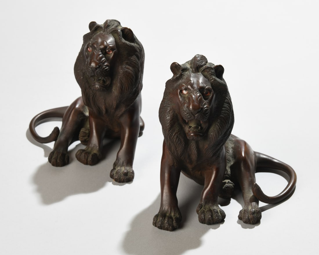 A Pair of Japanese Bronze Figures of Lions: Late Meiji / Taisho period (early 20th century)Each realistically cast as a roaring male lion in a seated posture, the thick manes finely detailed with stylized fur, the eyes inlaid with glass giving 