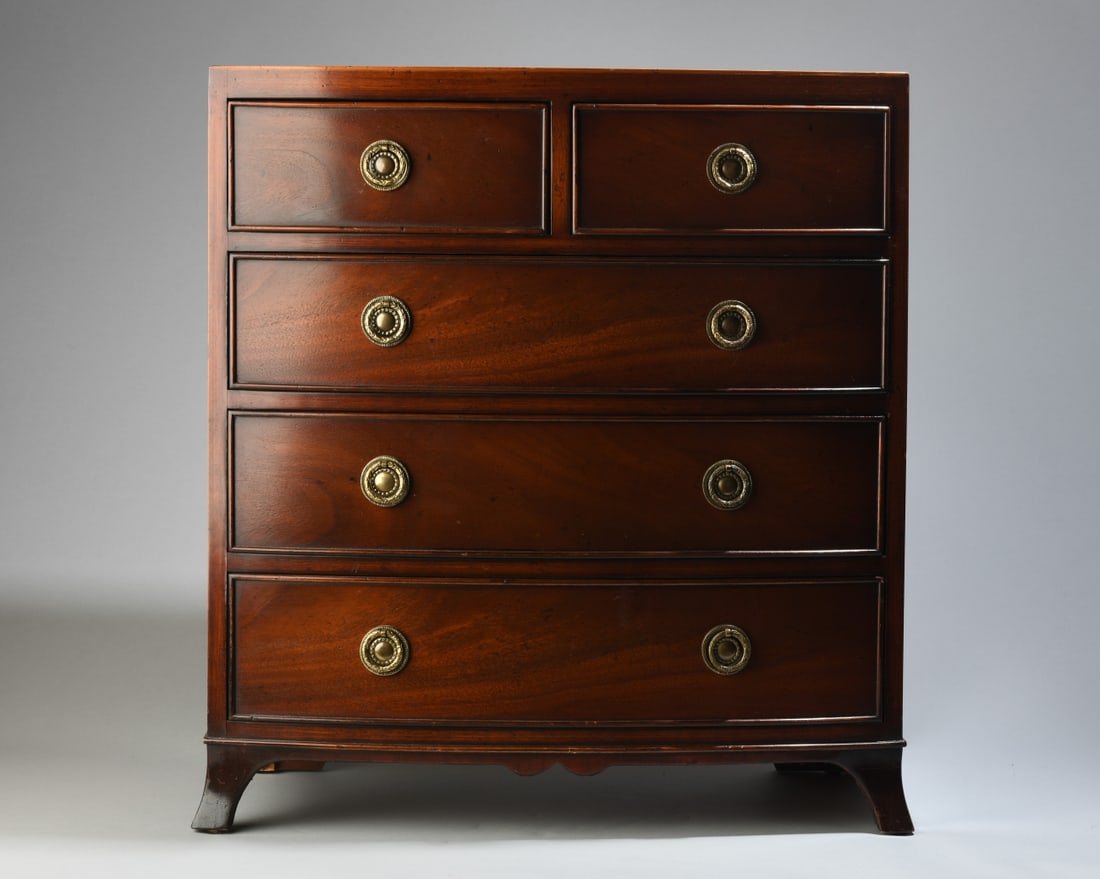 Yorkshire House Diminutive Chest of Drawers: Mahogany, bowfront case with two short dovetailed drawers with brass pulls over three long drawers, curved feet, label to drawer interior. H: approx. 24". W: approx. 21 3/4". D: approx. 11". Our prima