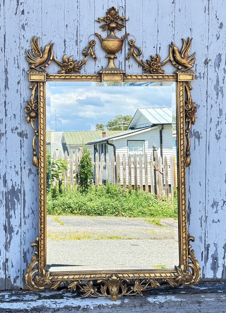 Vintage Federal Style Wall Mirror: A mid-to-late 20th-century Federal-style reproduction wall mirror. Features a gold-painted molded composition frame topped with a neoclassical urn finial, floral swags, and corner pheonixes over a rec