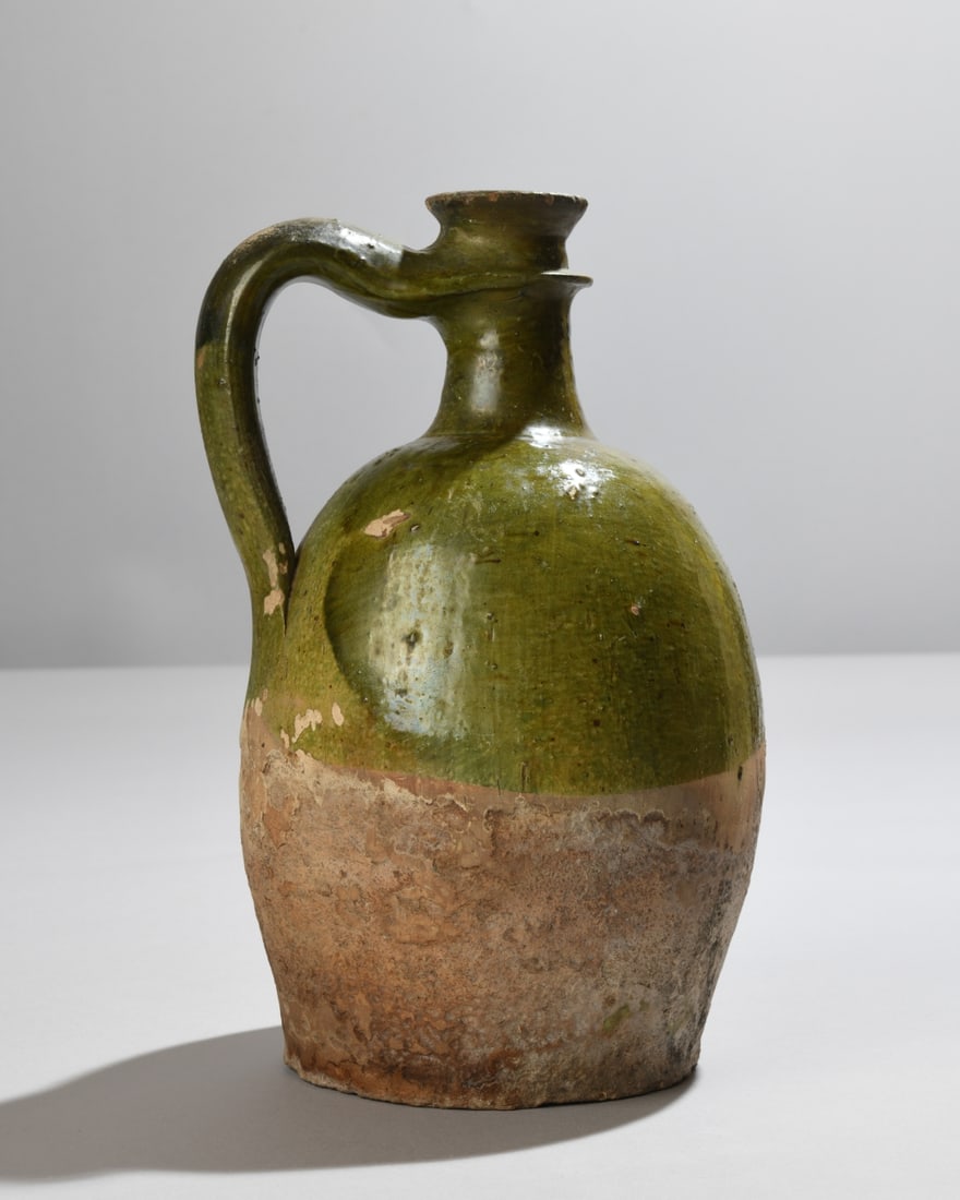 Antique French Green Glazed Olive Oil Jug: French green glazed earthenware oil jug with globular body, narrow neck, and high strap handle. Likely late 19th to early 20th century. Exhibiting surface wear, glaze losses, mineral accretions, and