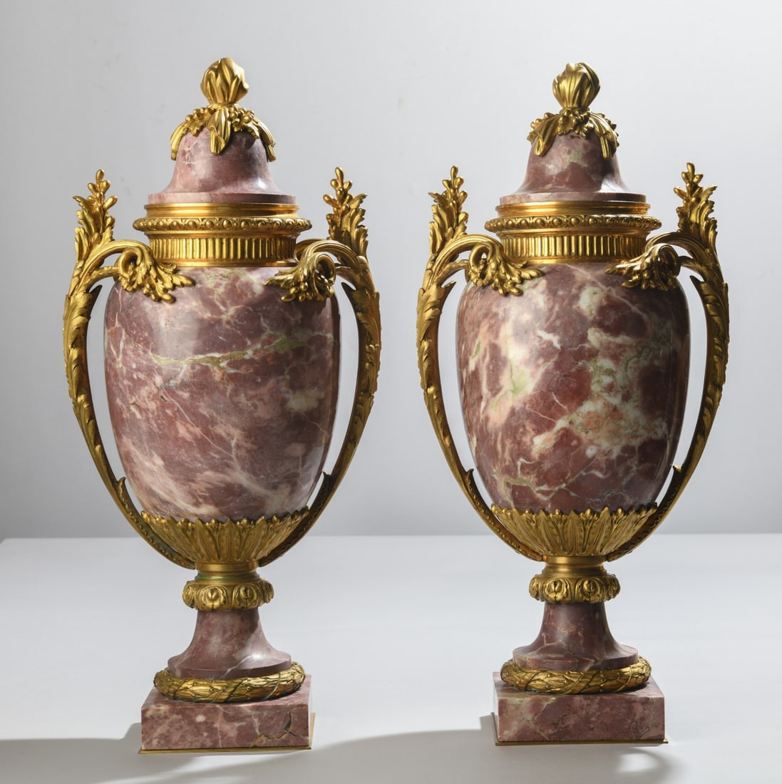 Pair Louis XVI Style Brèche Violette Marble Urns: Pair of Louis XVI style Brèche Violette marble urns with gilt bronze mounts. Featuring scrolling acanthus handles, fluted detailing, and foliate finials. Dimensions approx. 19 3/4" x 9" x 6". Our