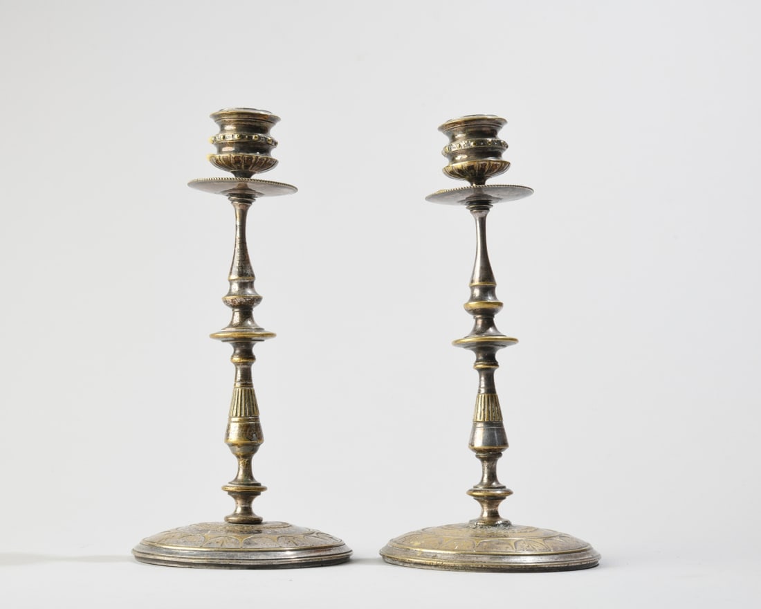 Pair of Continental Silvered Stems: Pair of Continental style silverplated or silvered brass candlesticks. Each features a slender baluster stem resting on a wide, circular domed base chased with a stylized petal or fan motif. No visibl
