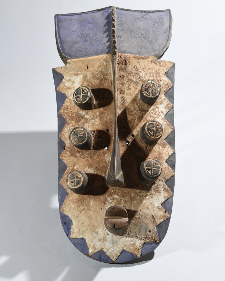African Grebo War Mask: longated projecting nose, three pairs of tubular eyes with incised geometric details, serrated facial borders, and broad divided crest, painted in muted blue-gray, black, and earthy tones. Approx. 23