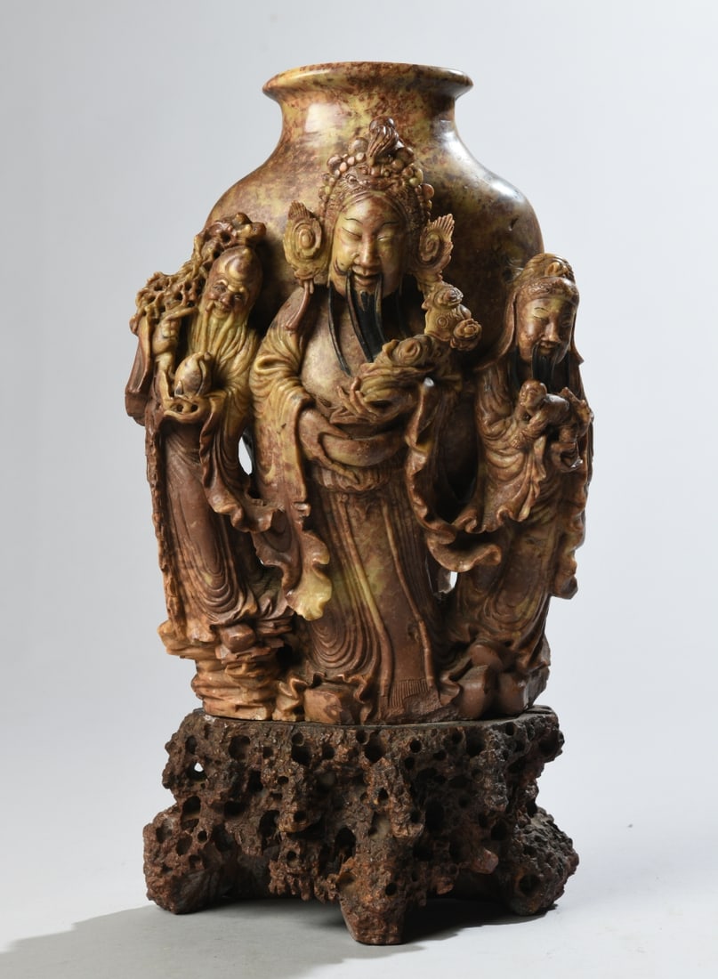 Chinese Carved Soapstone Figural Vase: Chinese carved soapstone vase with high-relief decoration of three robed figures, a child, and auspicious objects, on a rocky-form base. 20th century. Unmarked. Surface wear, some chips / losses, and