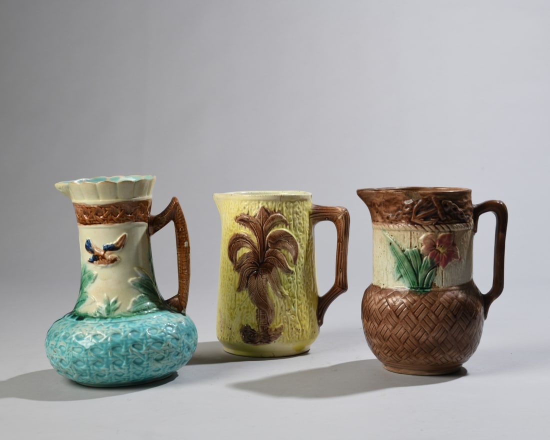 Three Late 19th / Early 20th C. Majolica Pitchers: Polychrome glazed earthenware pitchers including examples with floral, palm tree, bird and basket-weave decoration. Unmarked. Some chips and cracks / in as-found condition. Largest approx. 7 1/4" x