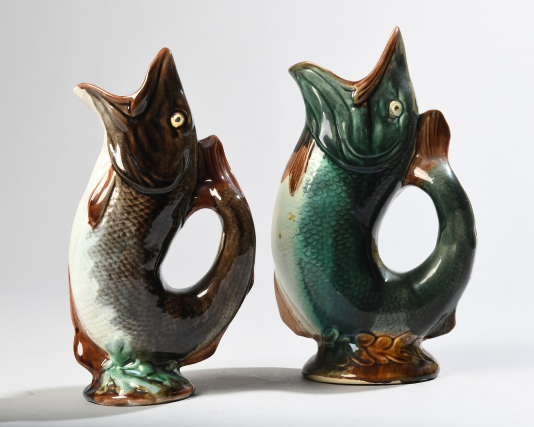 Pair of Majolica Fish Pitchers: Pair of graduated molded majolica pitchers modeled as upright fish, with open mouths forming the spouts and curled tails forming handles. Larger pitcher with hairline down the belly. Largest: approx. 