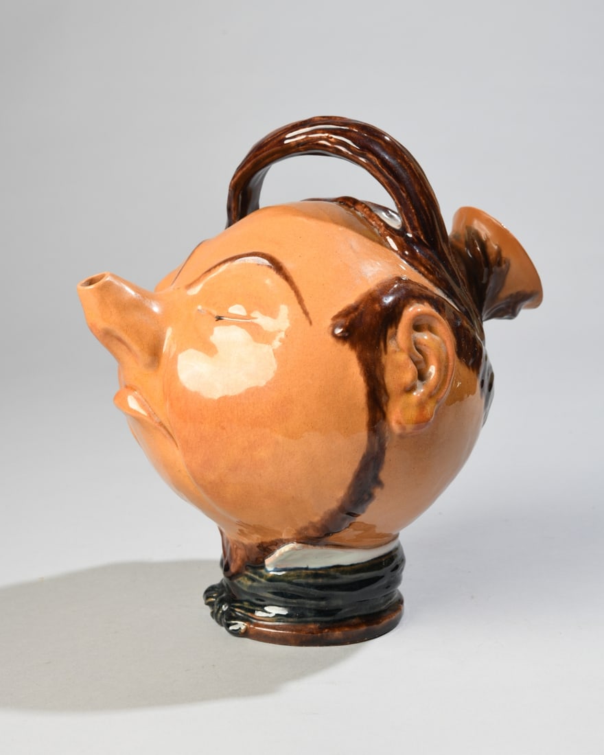 Portuguese Figural Novelty Jug: 20th century Portuguese glazed earthenware novelty jug modeled as a caricature male head with exaggerated pointed nose/spout, applied ears, dark brown hair and overhead handle. Underside impressed