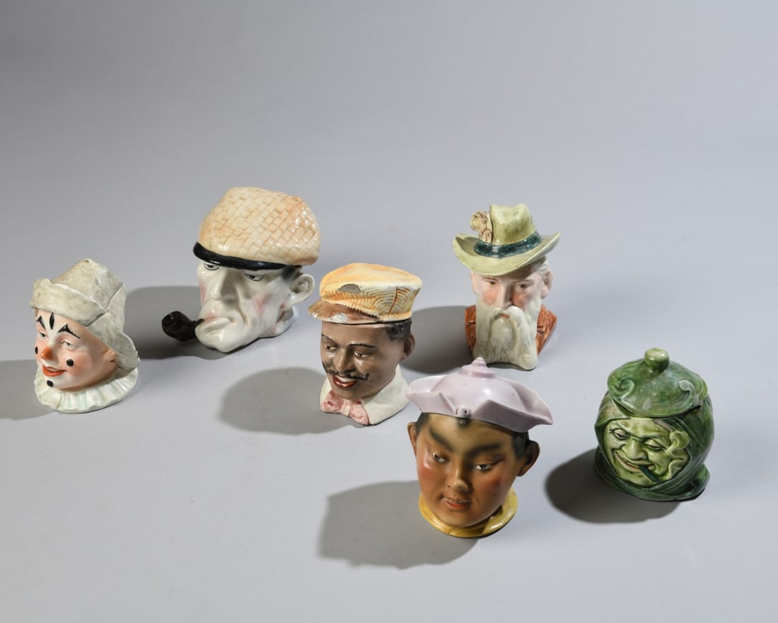 Six Figural Tobacco Jars: Late 19th / early 20th century figural ceramic tobacco jars, each modeled as a character head with removable lid, some with impressed numerals or faint underside markings. Some chips and cracks / all