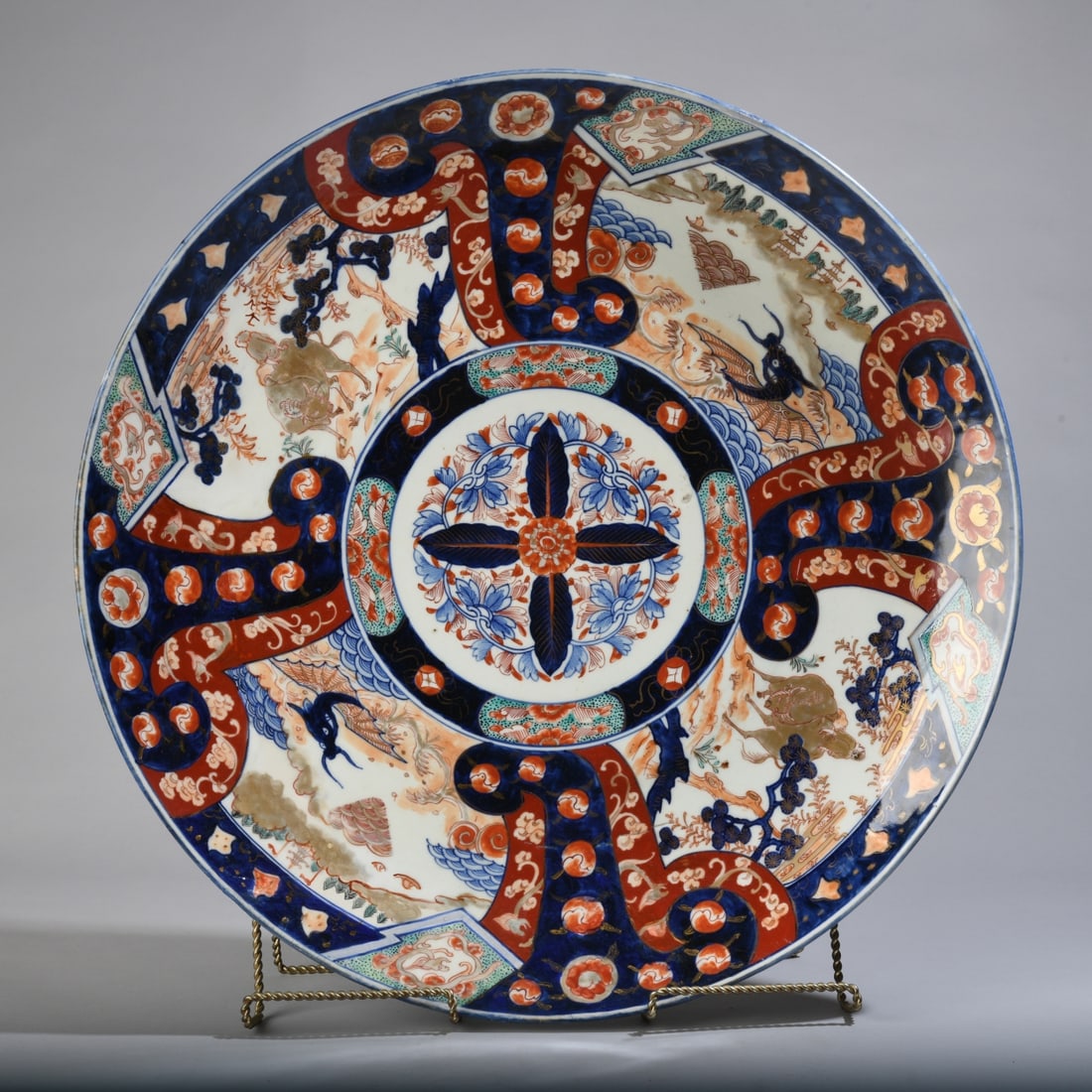 Monumental Japanese Imari Charger: Late 19th / early 20th century, with central floral medallion surrounded by densely decorated panels depicting dragons, figures, landscape elements, and stylized motifs. Underside with underglaze