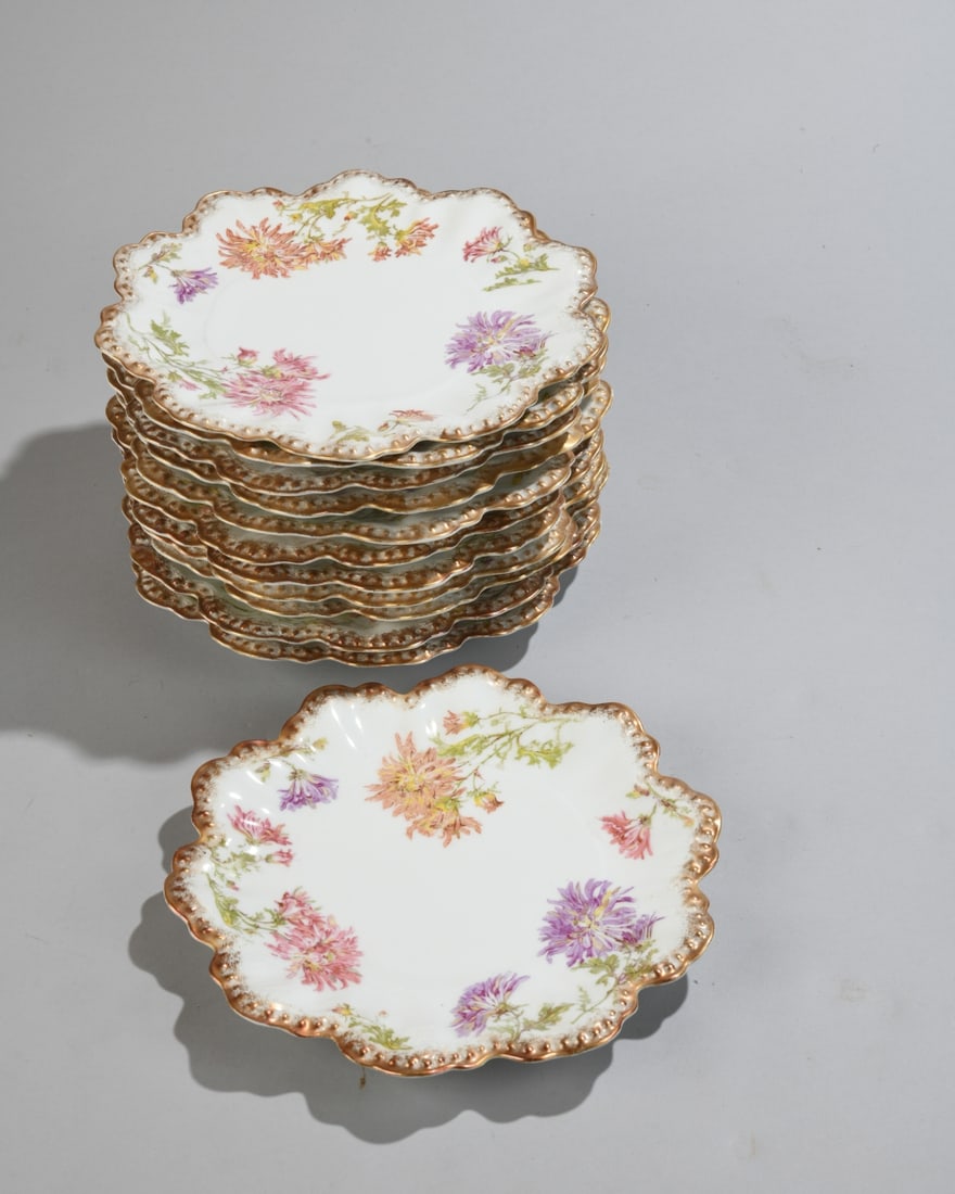 Set of 12 Limoges Porcelain Plates: Set of twelve porcelain plates with scalloped, gilt-beaded rims and scattered chrysanthemum decoration in pink, peach, and lavender on a white ground. Marked to underside for A. Lanternier, Limoges,
