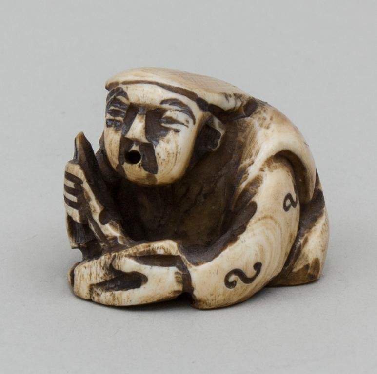 Netsuke Schreiber/Clerk, Japan, 19. Jh. Elfenbein,: Netsuke Schreiber/Clerk, Japan, 19. Jh. Elfenbein, braun patiniert. Gedrungen sitzender Mann mit Schreibstift und Tafel. Rücks. Kordellöcher (Himotoshi) und Dekoration des Gewands. Unters. Ritzsign.