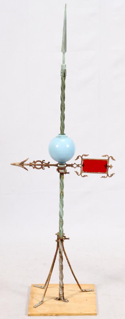ANTIQUE METAL LIGHTING ROD C1900: ANTIQUE METAL LIGHTING ROD, C1900, H 52", W 18":Having a copper spiral design shaft with scroll form arrow with red glass insert. Powder blue glass insulator ball. Tripod legs and mounted on a plywood