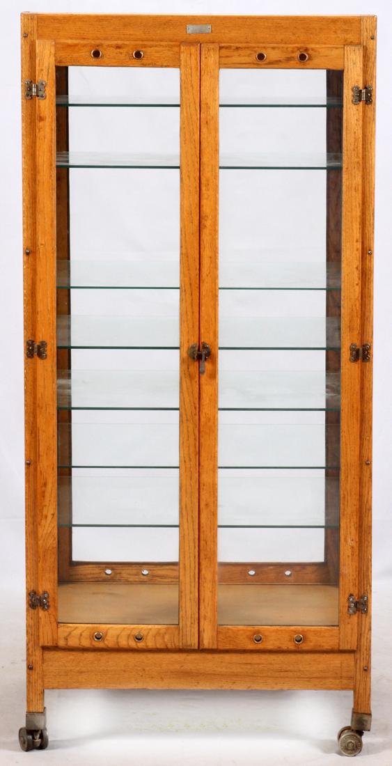 MIAMI MANUFACTURING CO. OAK PHARMACY CABINET: MIAMI MANUFACTURING CO. OAK, PHARMACY CABINET, H 66", W 30":Stamped to wheels: "Run Rite Hamilton Caster Mfg. Co." Oak framed glass construction with two full width cabinet doors opening to seven glas