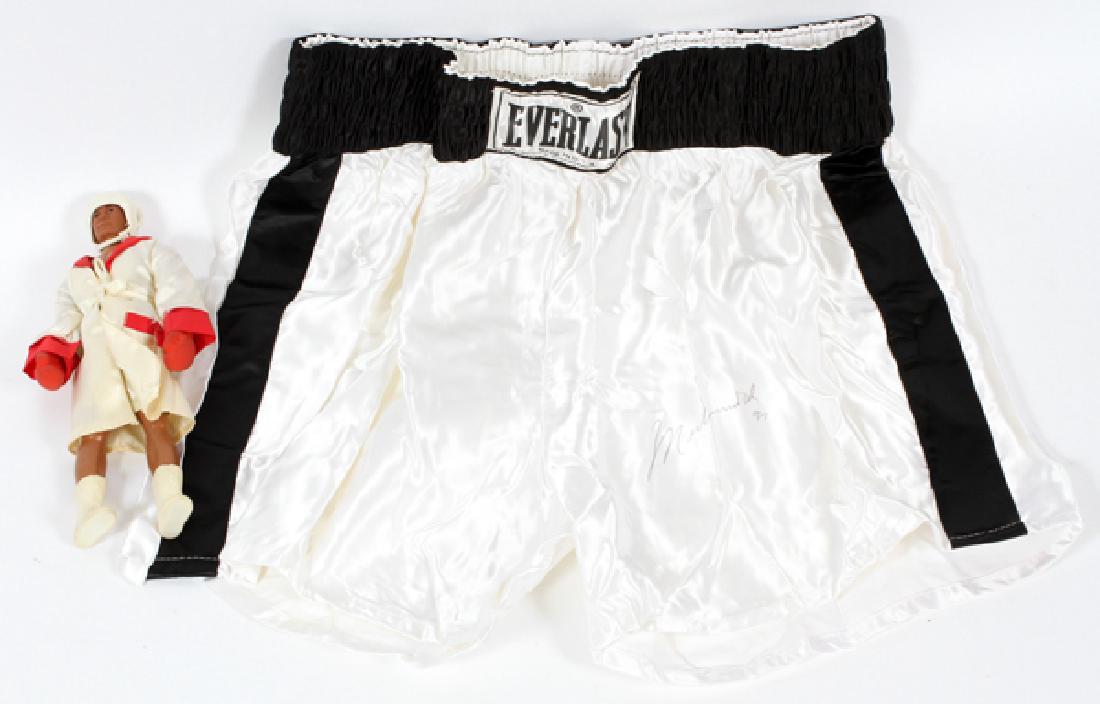 MUHAMMAD ALI AUTOGRAPHED BOXING TRUNKS: MUHAMMAD ALI AUTOGRAPHED BOXING TRUNKS AND UNSIGNED DOLL, 1974 & 1997, 2 PCS. H 10" (DOLL):Includes: one pair of "Everlast" white boxing trunks autographed and dated: "Muhammad Ali '97" and a miniatur