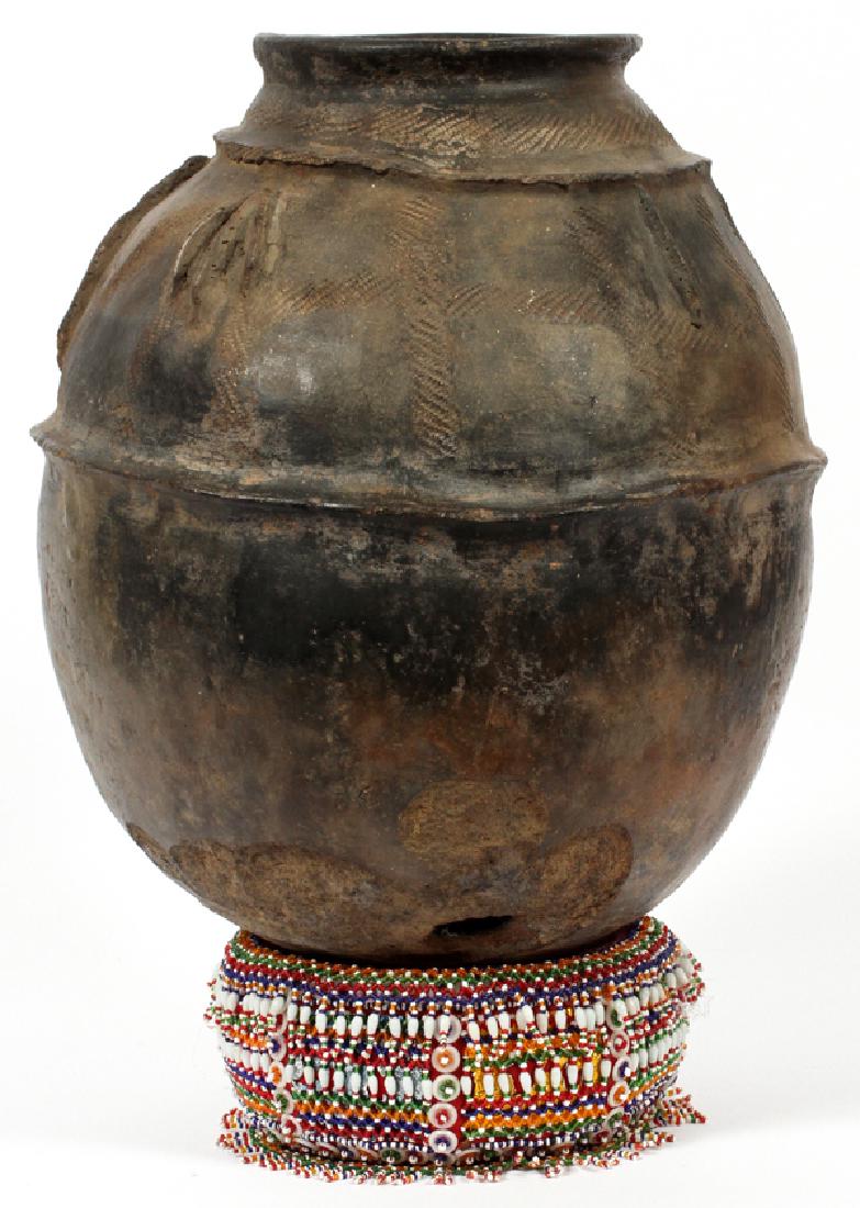 AFRICAN EARTHENWARE VESSEL: AFRICAN EARTHENWARE VESSEL, H 14", DIA 11":Having a bulbous body with incised and banded decoration to exterior, raised on a beaded circular pillow. Label to underside reads "African oil jar".