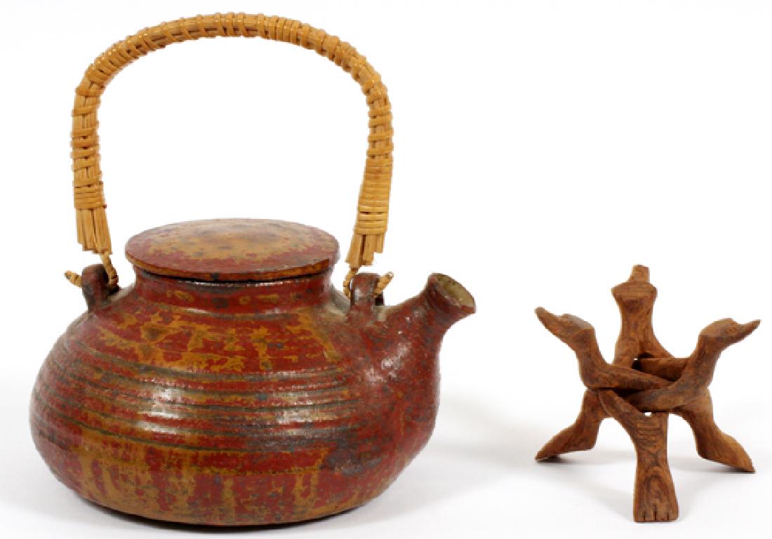 HEIJU OAK PACKARD POTTERY TEA POT: HEIJU OAK PACKARD POTTERY TEA POT, H 4'', W 6 1/2'' TEAPOT WITH REED HANDLE AND RED GLAZE. POT IS SIGNED "OAK" ON UNDERSIDE. MEASURES: H 4'', L 6 1/2''. HEIGHT ON STAND MEASURES: 6 1/2''.