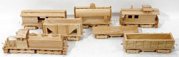 CARVED OAK TOY TRAIN, C.1993, 7 PCS.: CARVED OAK TOY TRAIN, C 1993, 7 PCS., H 1 3/4"- 6", L 10 1/2"-15":having Diesel locomotive, tank car, flatcar, gondola, hopper car, box car & caboose; brass couplers; signed "John Coblentz 6-22-93" on